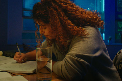 Diverse female studies in dorm room lit by desk lamp.