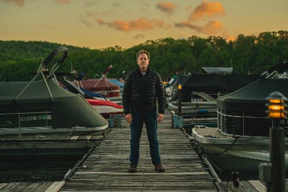 Man stands on dock lined with boats during sunrise.